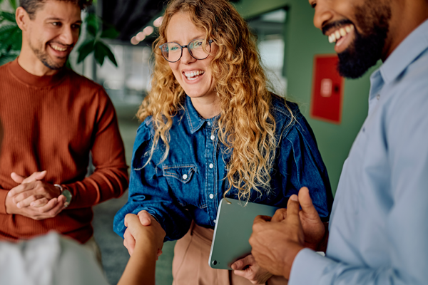 Three coworkers smiling and talking during a workplace meeting.