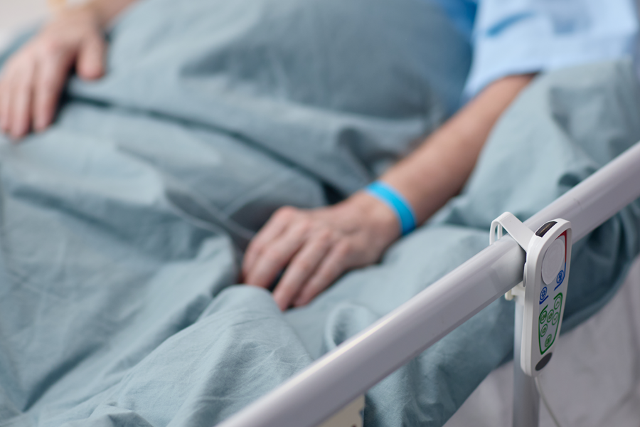 Close-up of a patient resting in a hospital bed with a bed rail and call button visible, symbolizing inpatient care, medical recovery, or hospitalization.